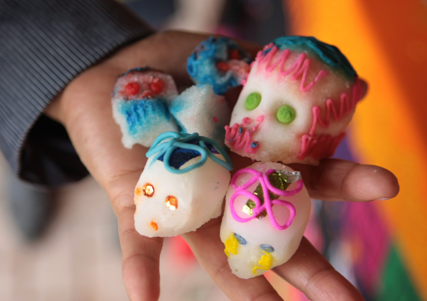 Small hand hold three small sugar skulls and three larger sugar skulls.